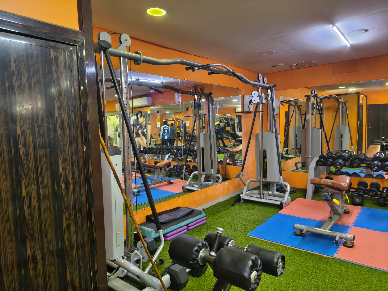 Cable crossover station on turf with step platforms, a hyperextension bench and dumbbell racks behind
