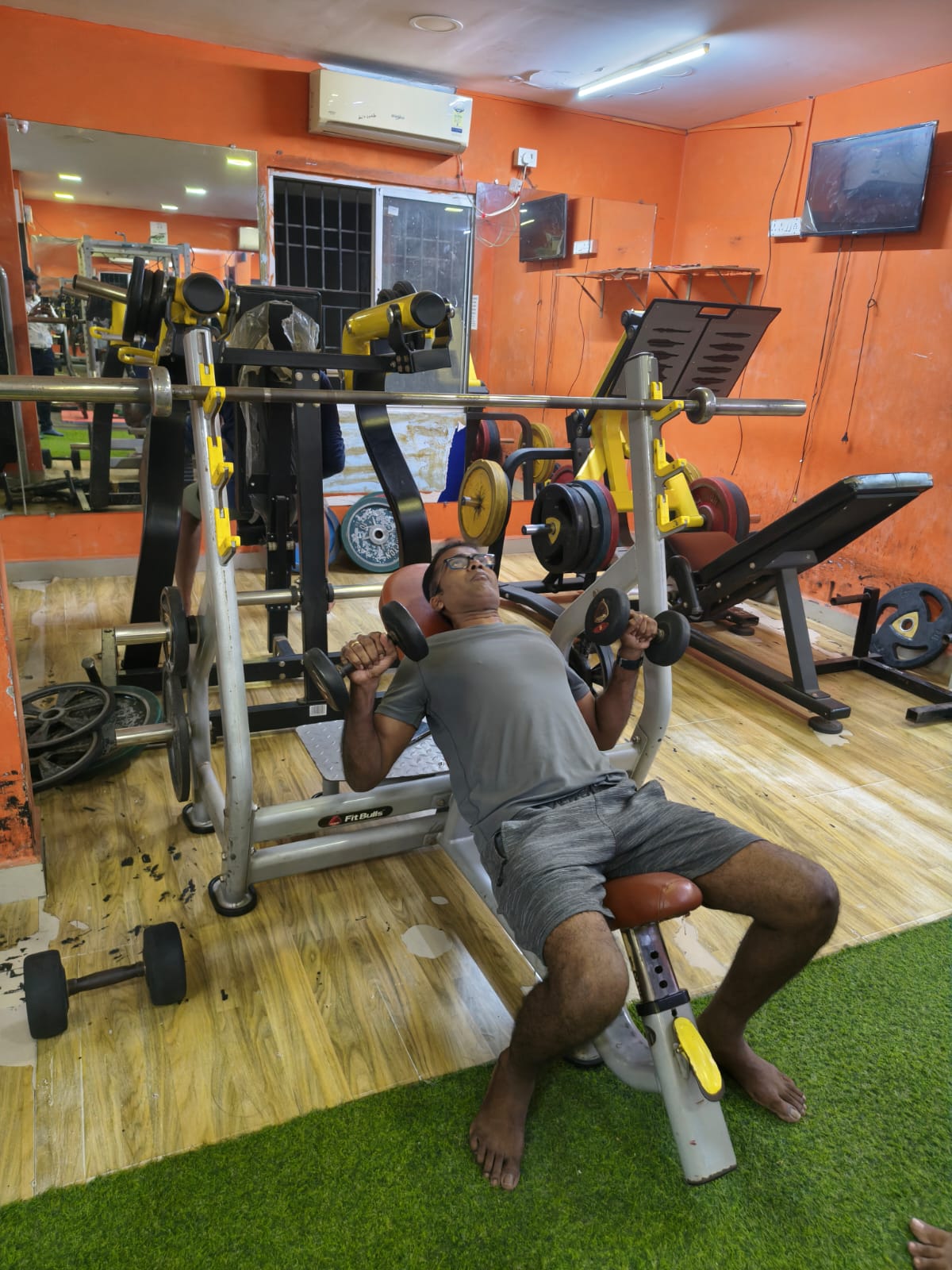Member doing an incline dumbbell press at Shree Fitness, with plate-loaded machines behind