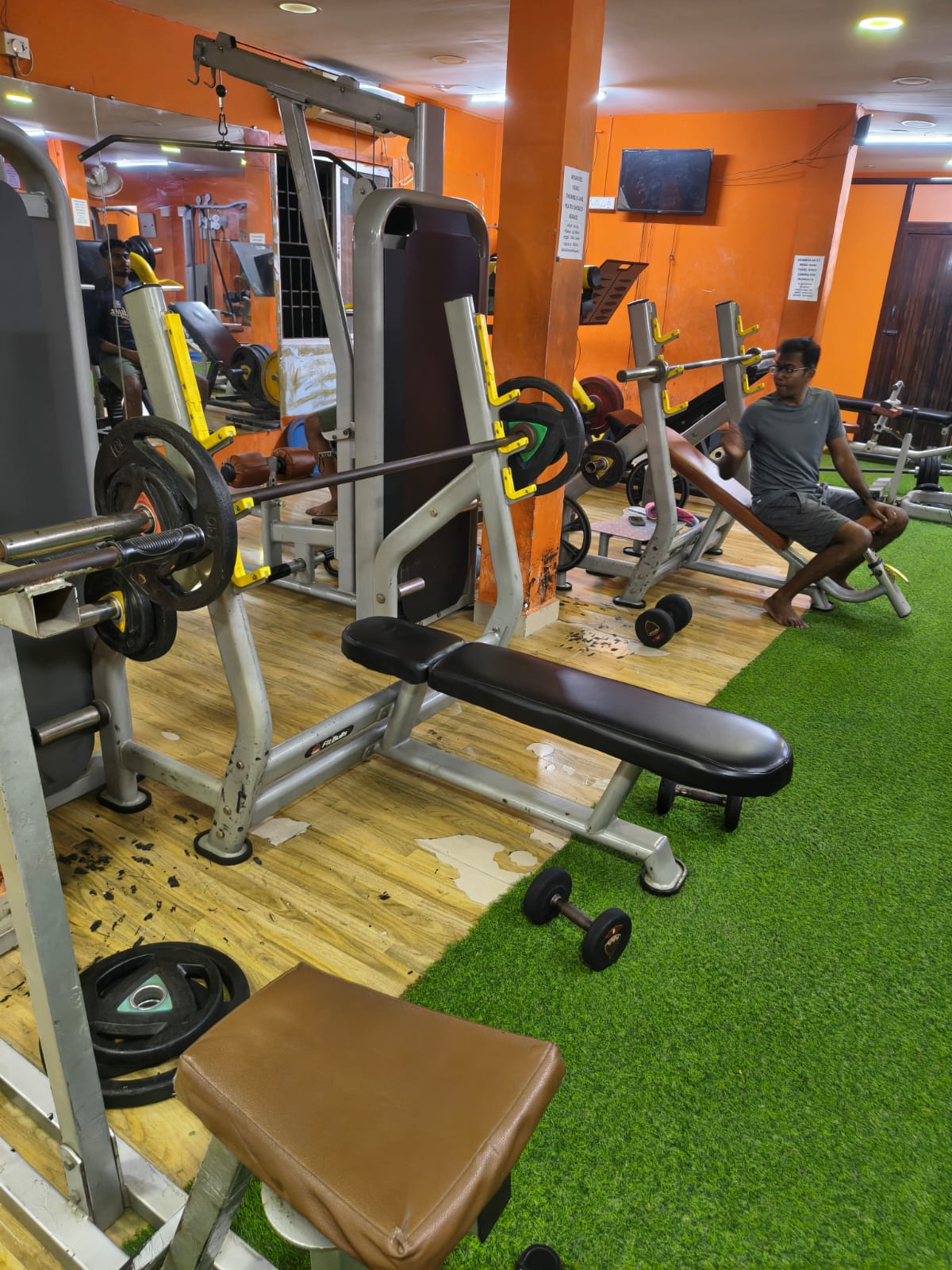 Flat and incline Olympic bench press stations beside the turf lane, with a lat pulldown behind