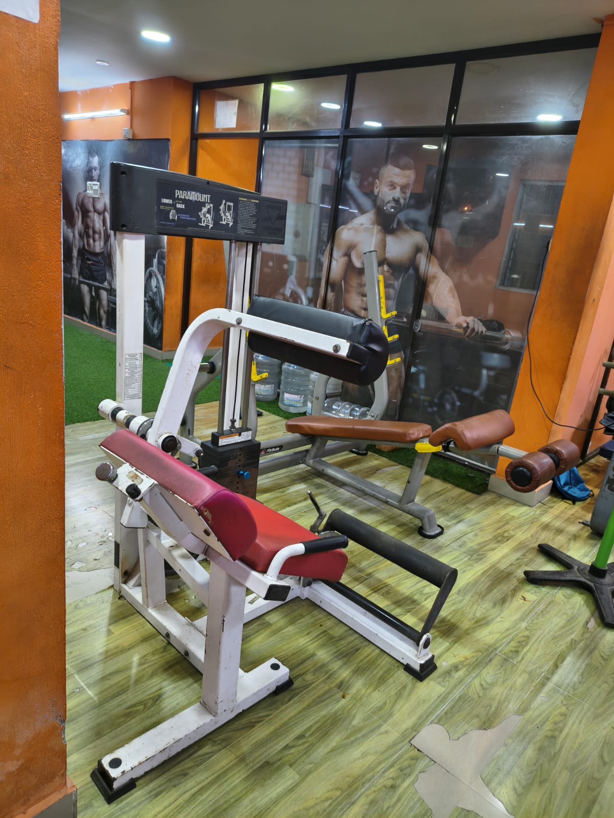 Lower back extension machine and leg extension bench in front of glass panels with fitness murals