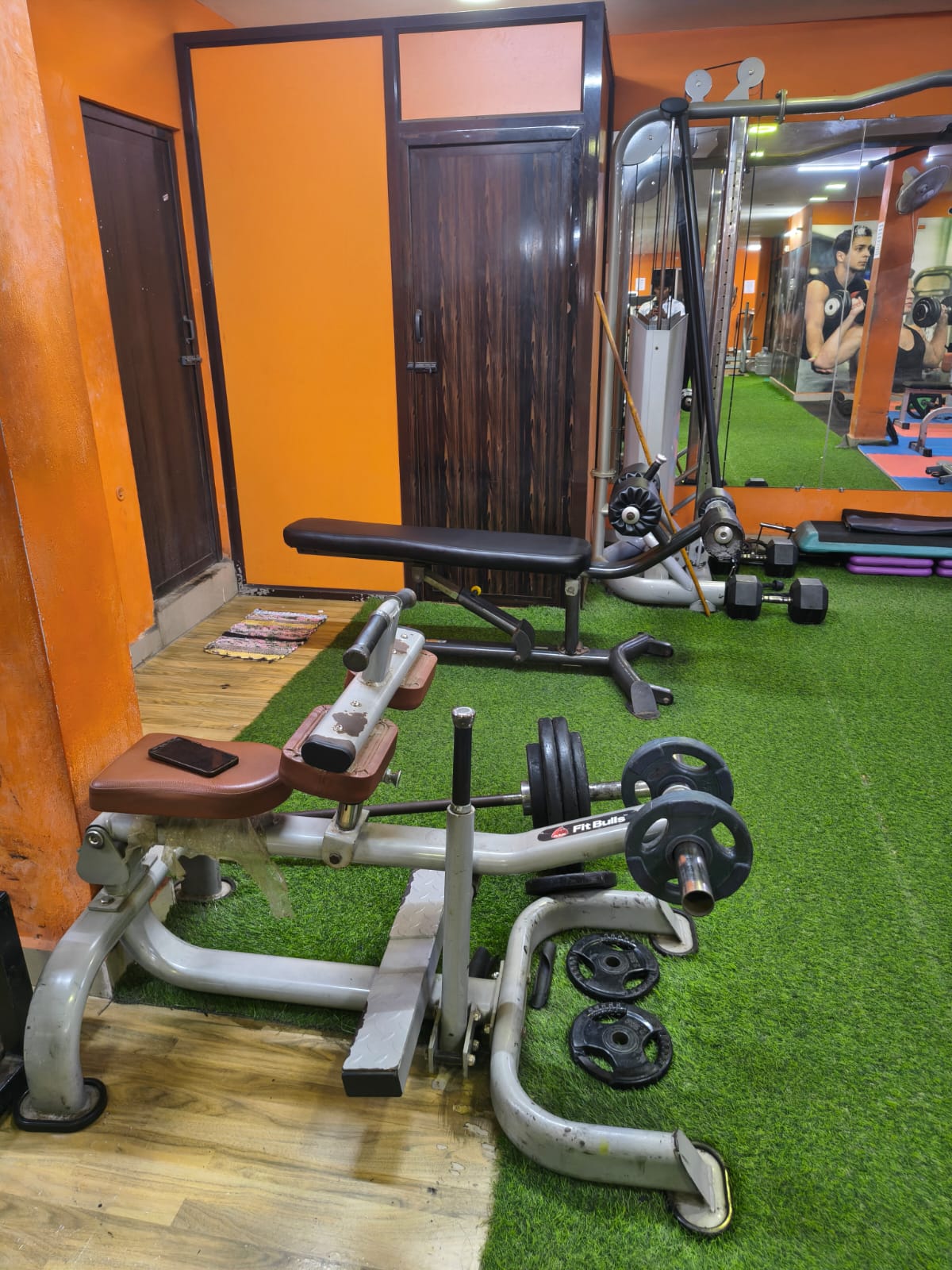 Plate-loaded seated calf raise, adjustable bench and dumbbells on green turf beside a cable station