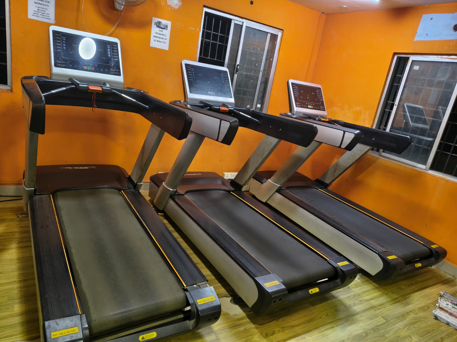 Row of three treadmills in the Shree Fitness cardio area, along an orange wall with windows