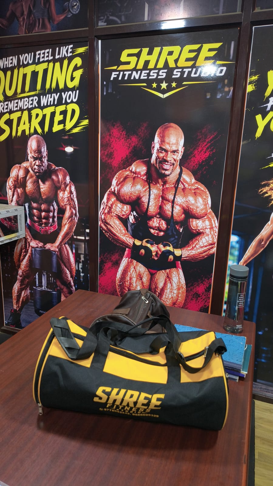 Black and yellow Shree Fitness Studio duffel bag in front of motivational posters