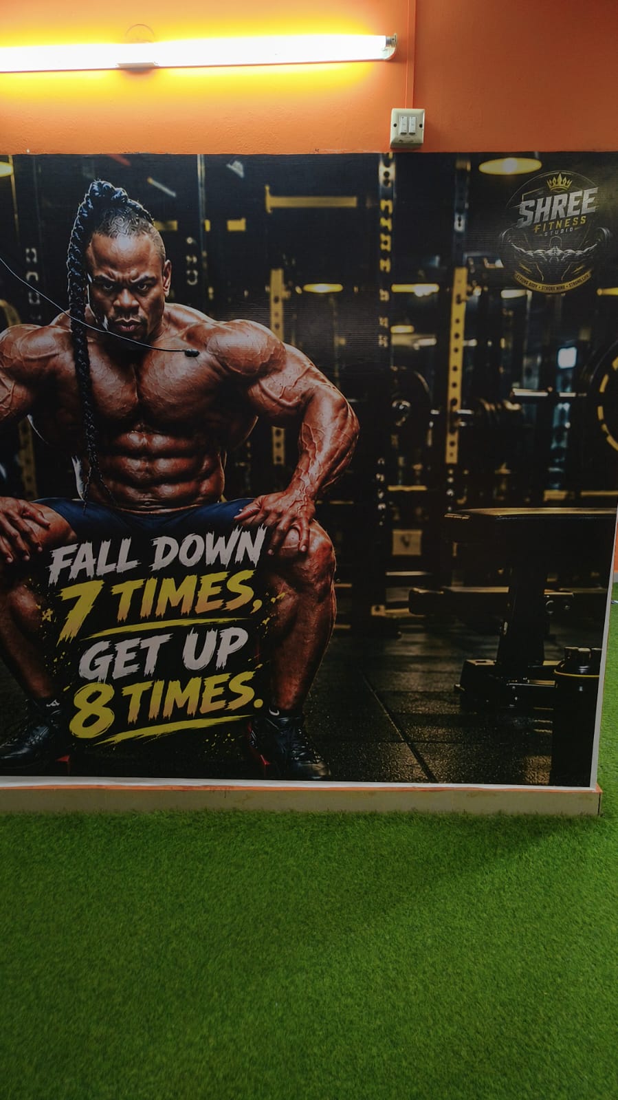 Wall mural reading “Fall down 7 times, get up 8 times” above the green turf training area